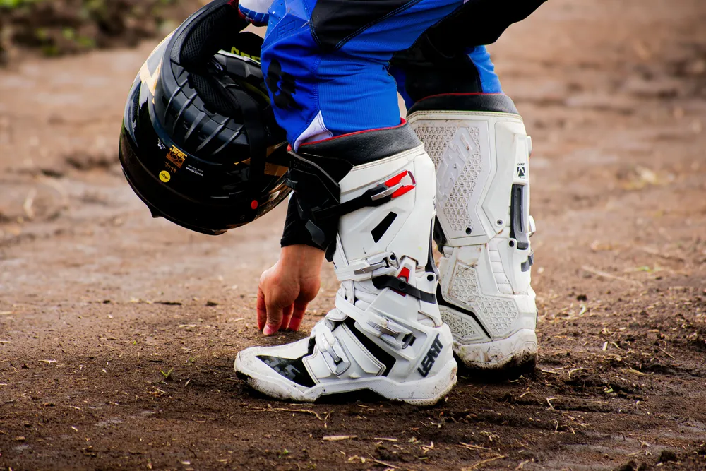 Motocross rider wearing protective boots and holding a helmet